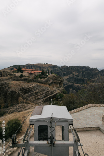 3rd person view of cable cart lines going across to other side showing nature mountains and old monasteries buildings hidden away in trees. cloudy skies europe greece