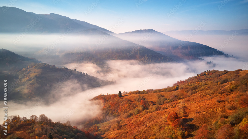 Beautiful Autumn mountain panorama. Morning thick fog cover valley