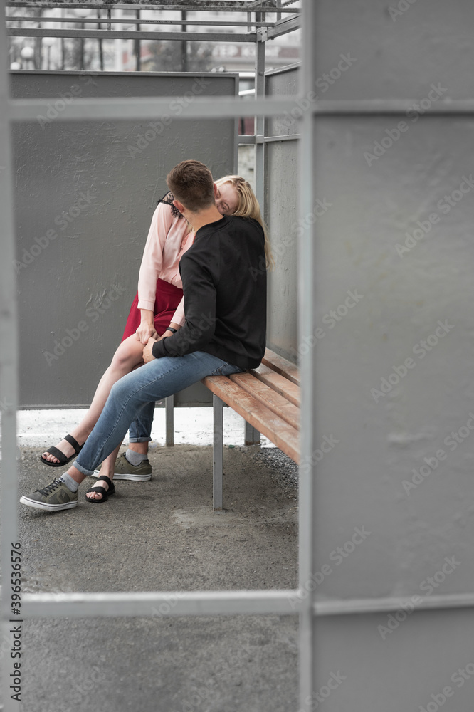 Young couple kissing sitting at bench at bus stop Young couple kissing sitting at bench at bus stop