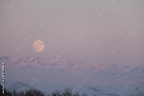 The full moon ascending over snowy mountains