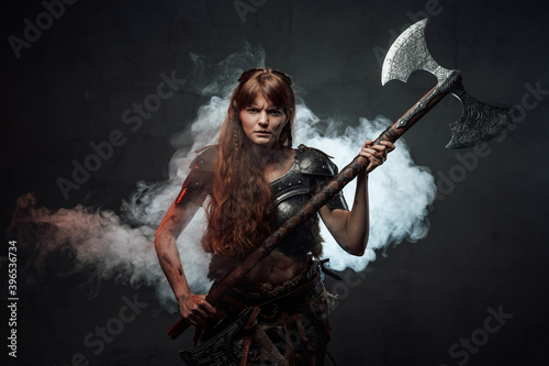 Violent and savage scandinavian female warrior holding huge two handed axe in dark foggy background. © Fxquadro