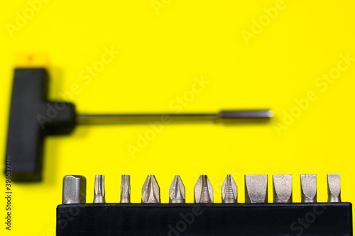 A set of screwdriver nozzles and a screwdriver on a yellow background with space for copyspace text. Tools for construction and repair shop