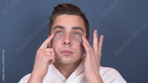 A young man with patches on his face relaxes. Spa treatments. Blue hydrogel patches for facial rejuvenation. A man is sitting in a white coat. Close-up photo