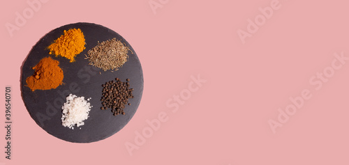 Various spices sea salt, black peppercorns, paprika, tumeric on round shale palette on pink background.  Copy space. Banner.