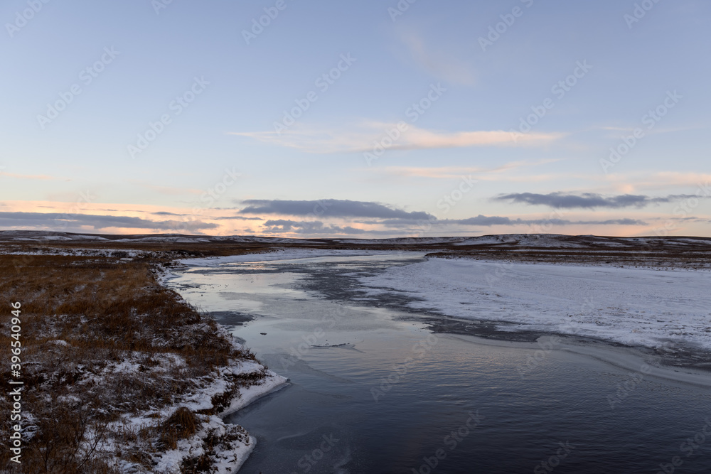 Arctic landscape in winter time. Small river with ice in tundra.