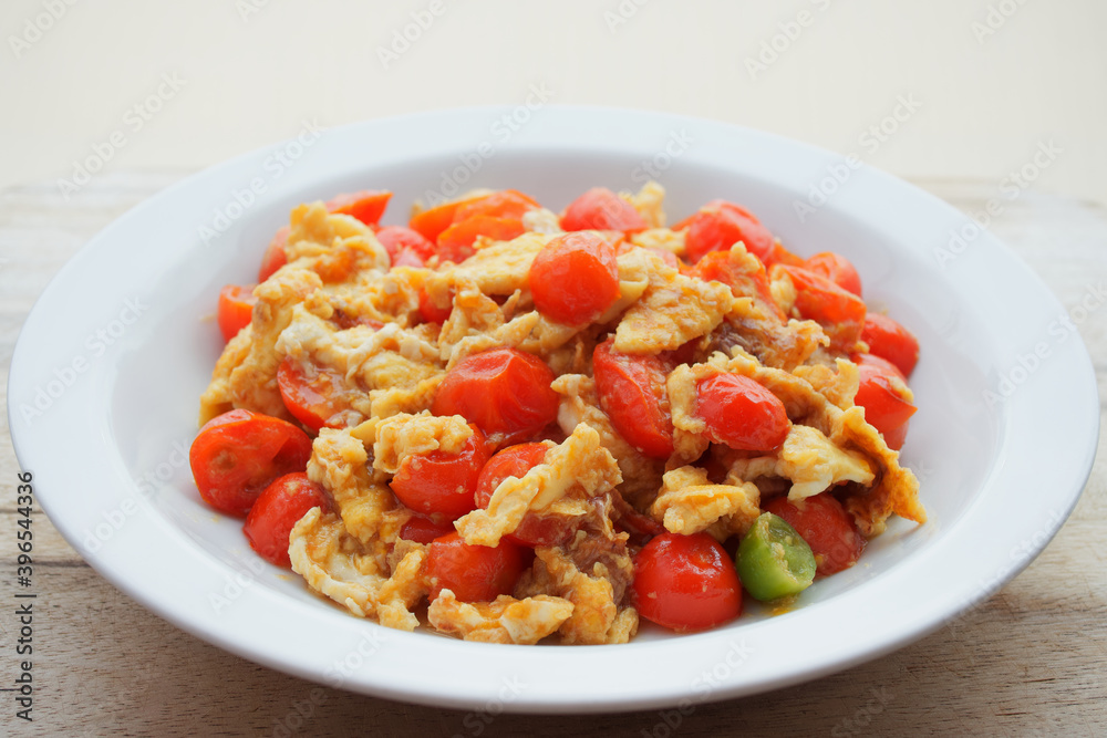 Tomato scrambled eggs in white ceramic dish on wooden table against blurred background with copy space. Tomato scrambled eggs in white ceramic dish on wooden table against blurred background with copy space.