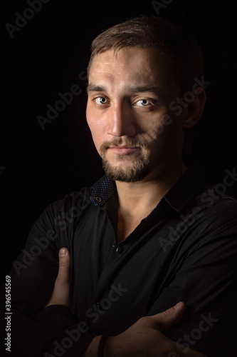 Closeup portrait of handsome man with a beard in black shirt. Isolated on black background