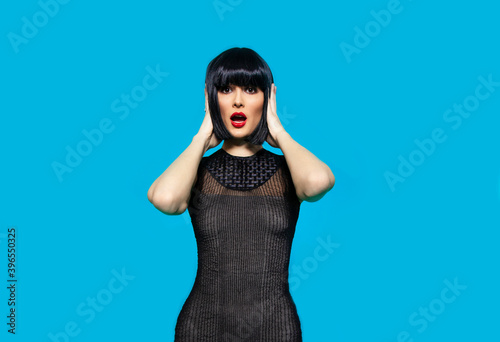 Front portrait of a surprised young beautiful dark-haired woman with red lip, over blue background. photo