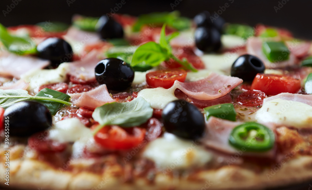 Pizza with ham, mozzarella cheese, cherry tomatoes, green and jalapeno pepper, black olives and fresh basil. Dark background. Close up. Pizza with ham, mozzarella cheese, cherry tomatoes, green and jalapeno pepper, black olives and fresh basil. Dark background. Close up.