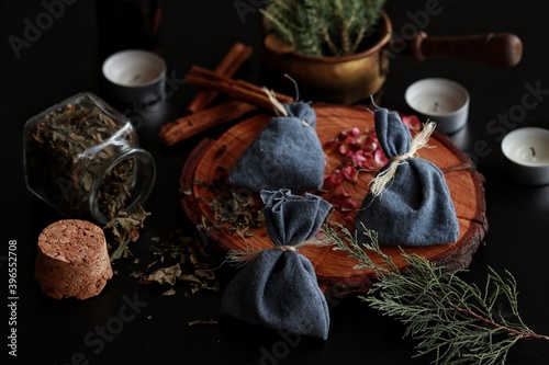 Yule winter solstice (Christmas) celebration themed magick spell bags made from blue cotton tied with yarn, filled with various herbs, spices. Dark black background with evergreens rose petals candles photo