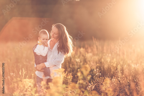 Beautiful sunny photo of motherhood, Caucasian mother with long hair in the summer at sunset with her son child in her arms. Back lighting, soft focus and toning, proximity