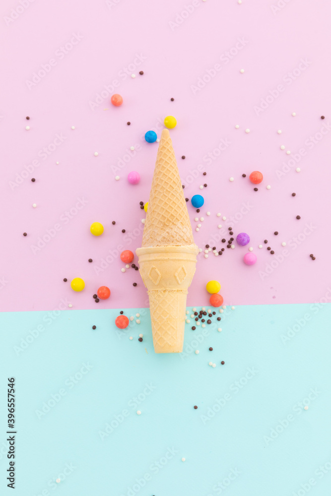 Two ice cream cones and scattered colourful sprinkle on pink and blue background
