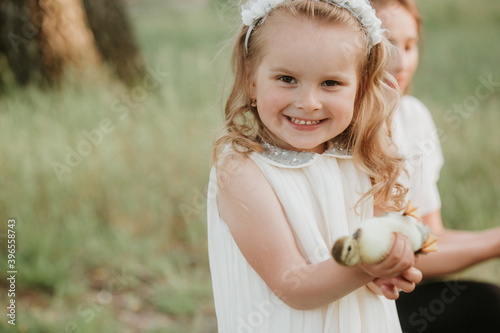 smiling little girl is holding a yellow duckling in her hand outdoors in summer in the green park.