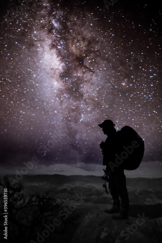 Silhouette of man with backpack and trekking poles against amazing Milky Way at night. Photographer and star in the night sky.