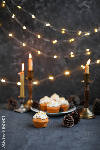 Muffins with butter cream in a vintage plate on a wooden high stand. New Year's festive desserts on the table with a garland and candles.