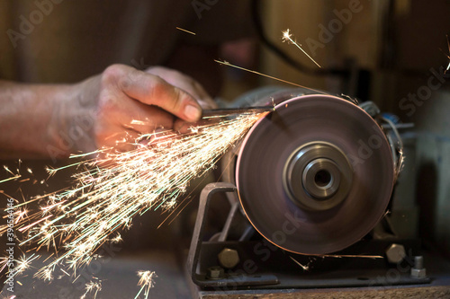 Man sharpens a metal blade on a machine. Man manufacturing in his workshop.