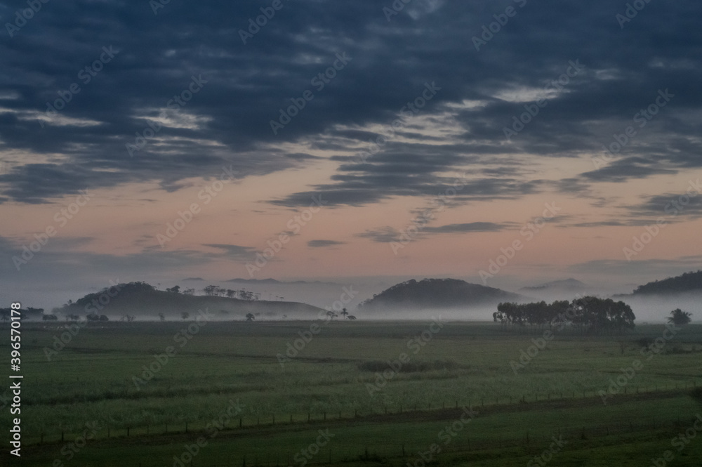mountains with fog in the background and a field of grass and clouds