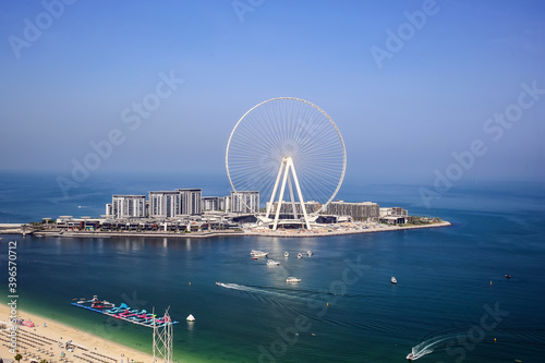 Dubai, UAE - 08.15.2020: Bright day view of white the largest ferris observation wheel - Dubai eye at Bluewaters island in the middle of sea gulf with boats and part of Jumeirah beach  © mynoemy1