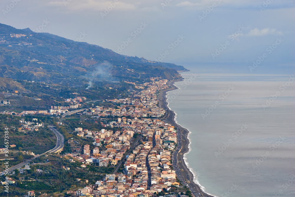 Fototapeta premium the eastern coast of Sicily seen from above with its towns, roads, railways, buildings and highways on a partially covered autumn day