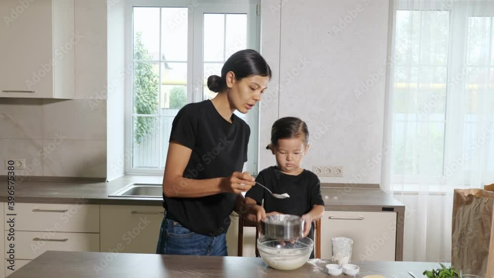 Mom and little daughter sift flour through a sieve into a bowl in the kitchen. Mom and little daughter sift flour through a sieve into a bowl in the kitchen.