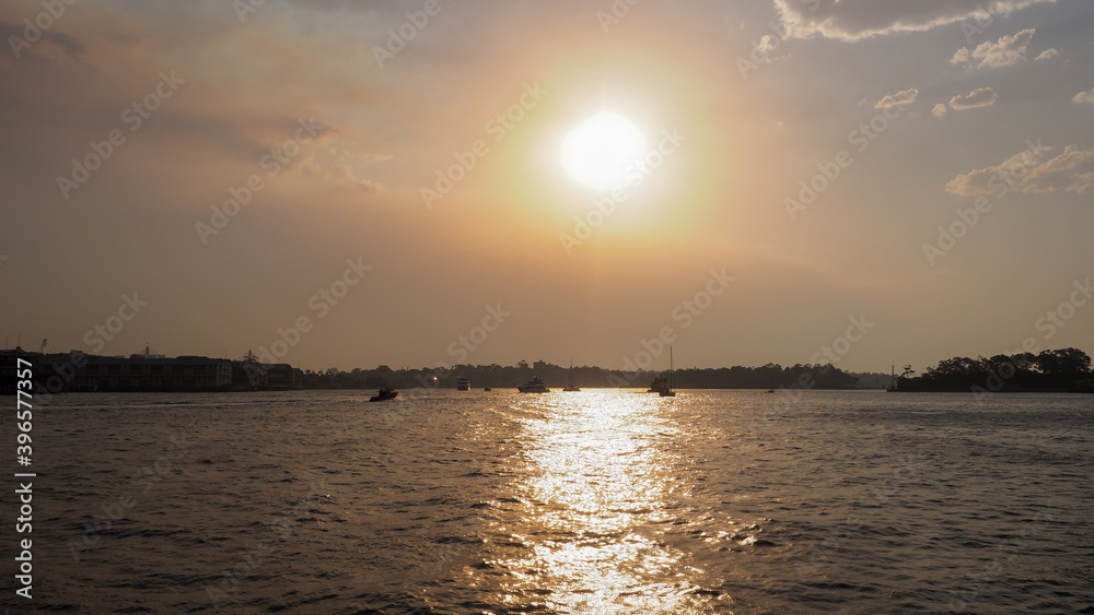 Sydney harbor view with orange sunset and silhouette of the boats and far islands.