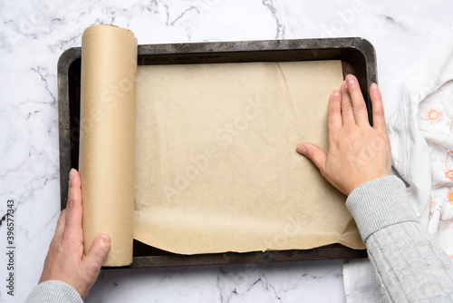 two female hands cover with brown parchment paper an iron rectangular baking sheet