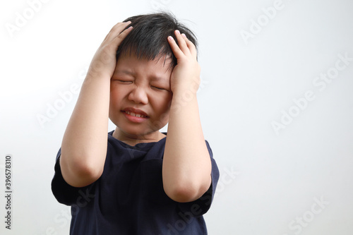 A frustrated Asian boy holding his head, standing against a light background.