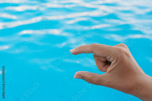 Closeup view horizontal photography of 1 female hand forming gesture as if showing size of virtual invisible object with help of two fingers isolated on bright blue blurry water of pool background.