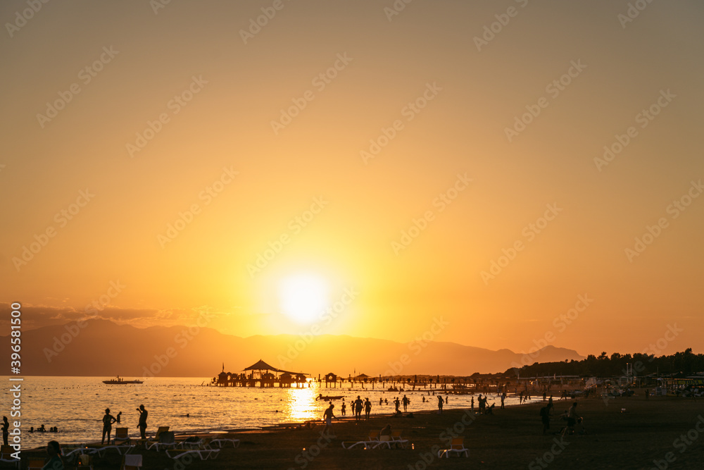 Black silhouettes of many people having fun on sunny sunset summer tropical beach during summer vacations