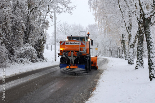 Snow plow is sprincling salt or de-icing chemicals on pavement in city.