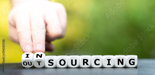 Hand turns dice and changes the word outsourcing to insourcing.