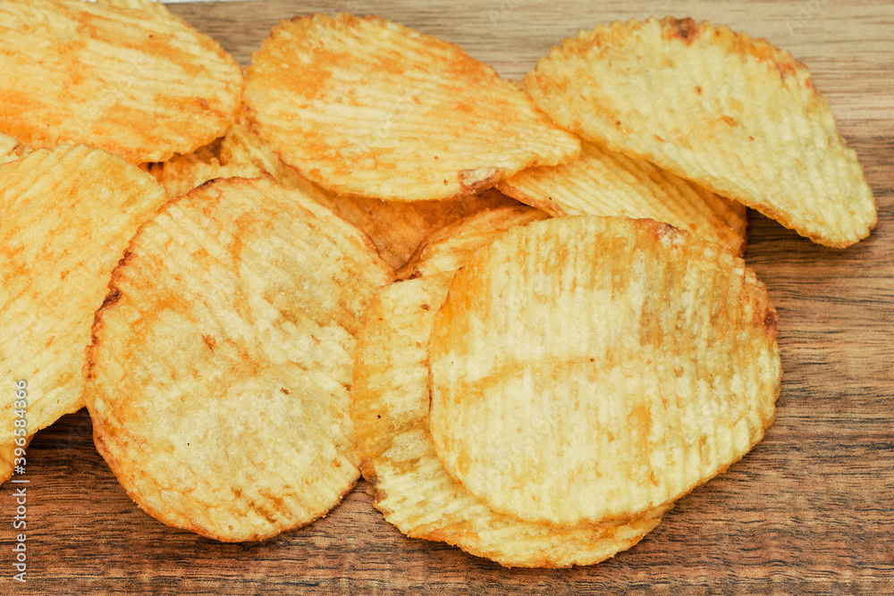 Corrugated potato chips on a wooden board. Snack, ready meal menu, junk food. Close up.