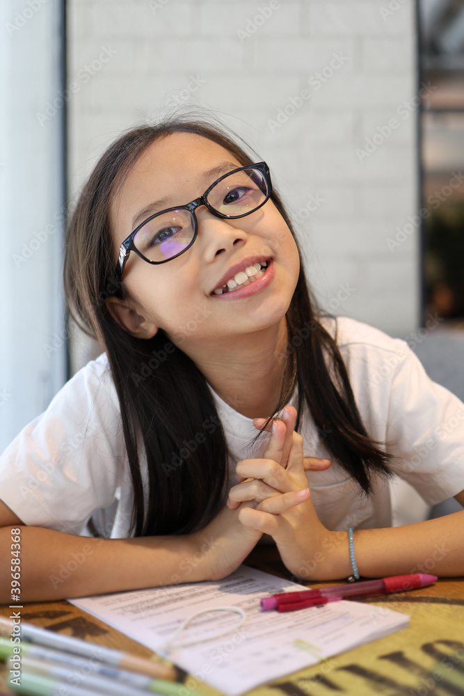 Portrait of cheerful 10-year-old Asian girl doing homework in the library, smiling and looking at the camera. Portrait of cheerful 10-year-old Asian girl doing homework in the library, smiling and looking at the camera.