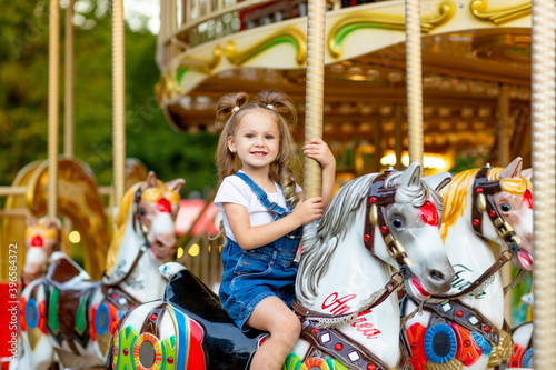 happy baby girl rides a carousel on a horse in an amusement Park in summer © Any Grant