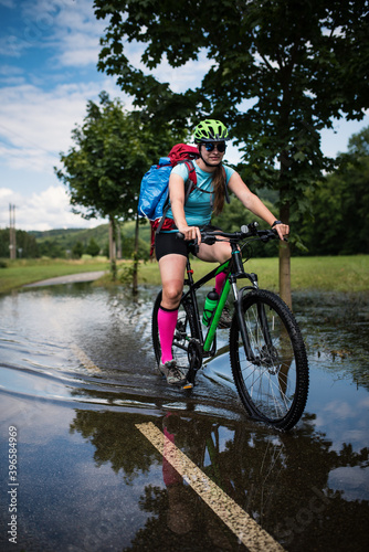 Fototapeta Naklejka Na Ścianę i Meble -  Young athlete woman riding a bicycle on a road through the water.