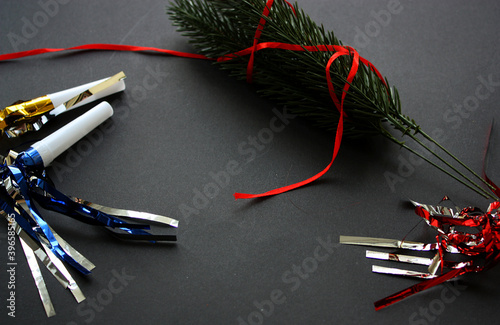 Winter holidays concept with spruce bouquet wrapped in red ribbon. Shiny festive air whistles. Black background. Christmas, New Year 2021 greeting card. Copy space.