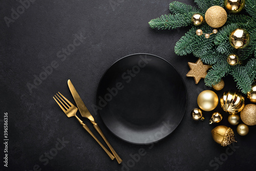 Christmas flat lay background with empty black plate, golden cutlery, christmas tree and toys. Top view, copy space. Trendy fashionable black theme Christmas, New Year table setting