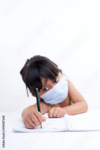Close-up little girl hand writing in notebook, Wearing a protective face mask