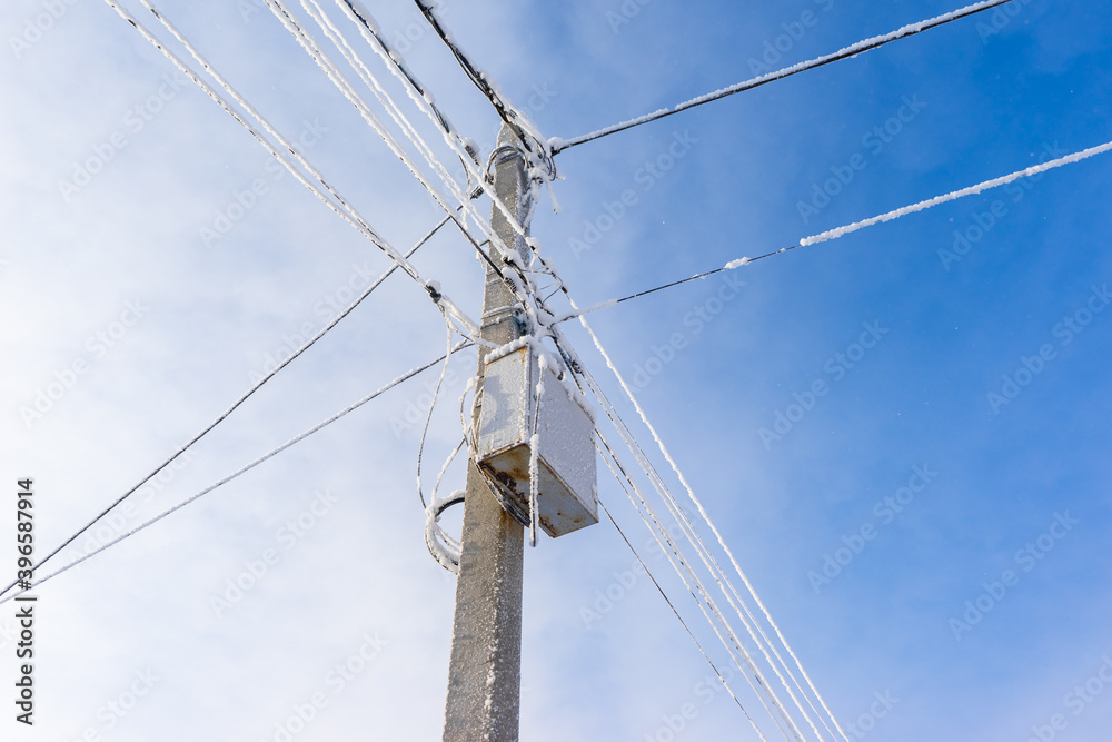 a pole with electric wires covered with snow and frost. frozen wires on the street. a pole with electric wires covered with snow and frost. frozen wires on the street.