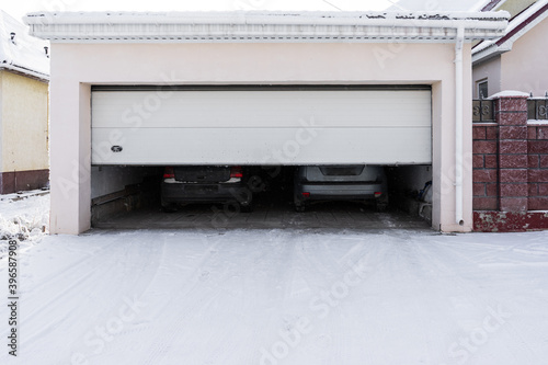xterior of a  garage attached to a house. garage with two cars inside in winter. semi-open sectional  doors