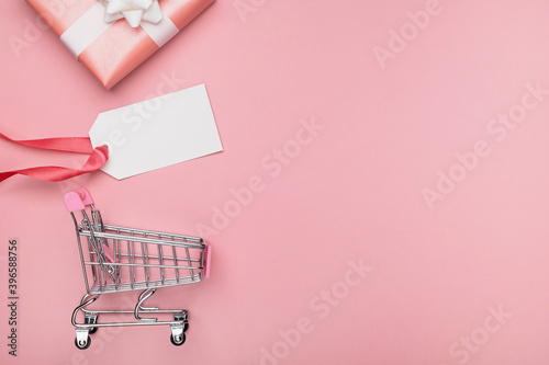 Sale, discounts and shopping concept. Miniature cart, gift box and empty tag card for text on pastel pink background. Top view, flat lay, copy space