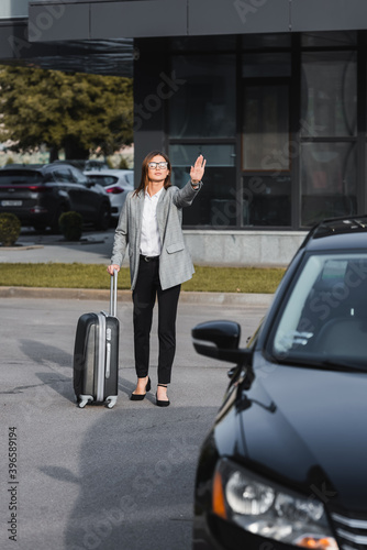  businesswoman with suitcase waving hand near black car on blurred foreground © LIGHTFIELD STUDIOS