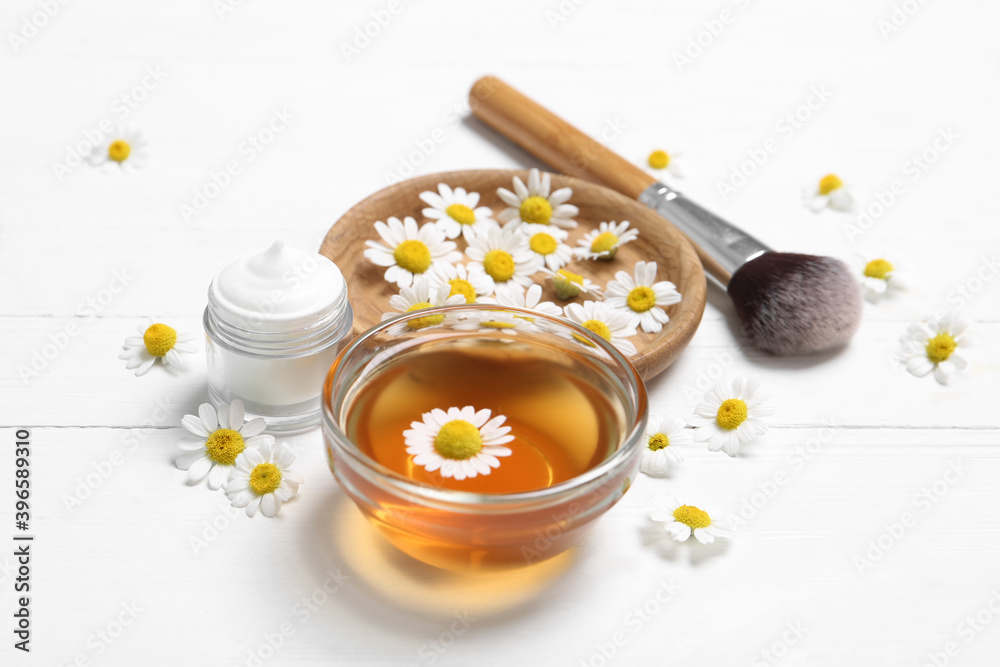 Composition with chamomile flowers and cosmetic products on white wooden table Composition with chamomile flowers and cosmetic products on white wooden table