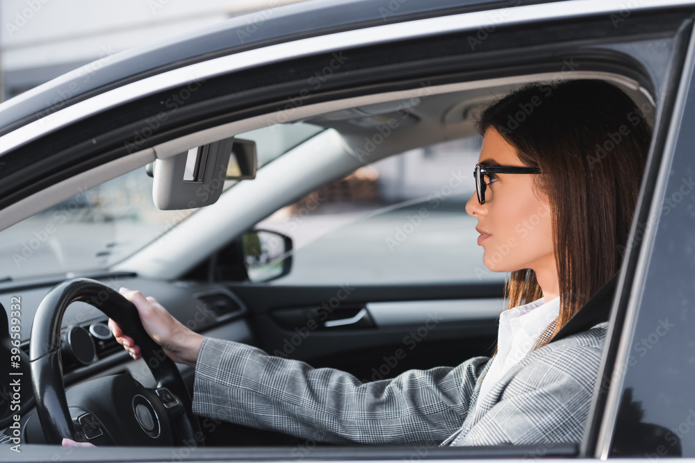 side of businesswoman in eyeglasses looking ahead while driving car