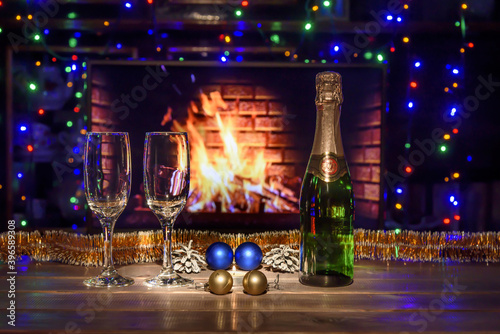 Two glasses and a bottle of champagne on the table. Christmas New Year decorations, fireplace. Fire, wood.