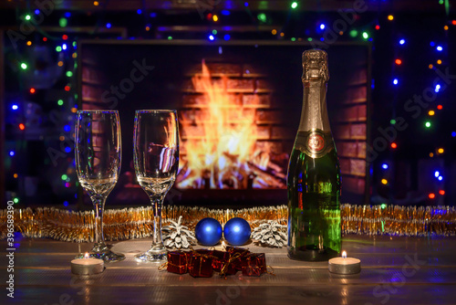 Two glasses and a bottle of champagne on the table. Christmas New Year decorations, fireplace. Fire, wood.