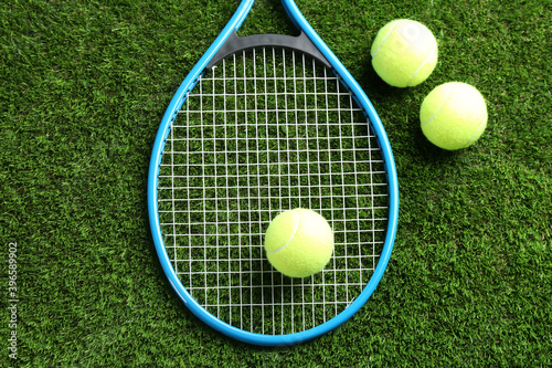 Tennis racket and balls on green grass, flat lay. Sports equipment