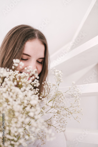 Portrait of young beautiful woman by the window with shadow from flowers on her face. Morning spring aesthetics.