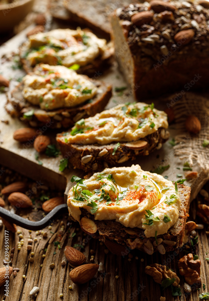 Buckwheat bread sandwiches with hummus and olive oil, sprinkled with chopped parsley and paprika powder on a board close-up.  Healthy vegan and gluten-free  food
