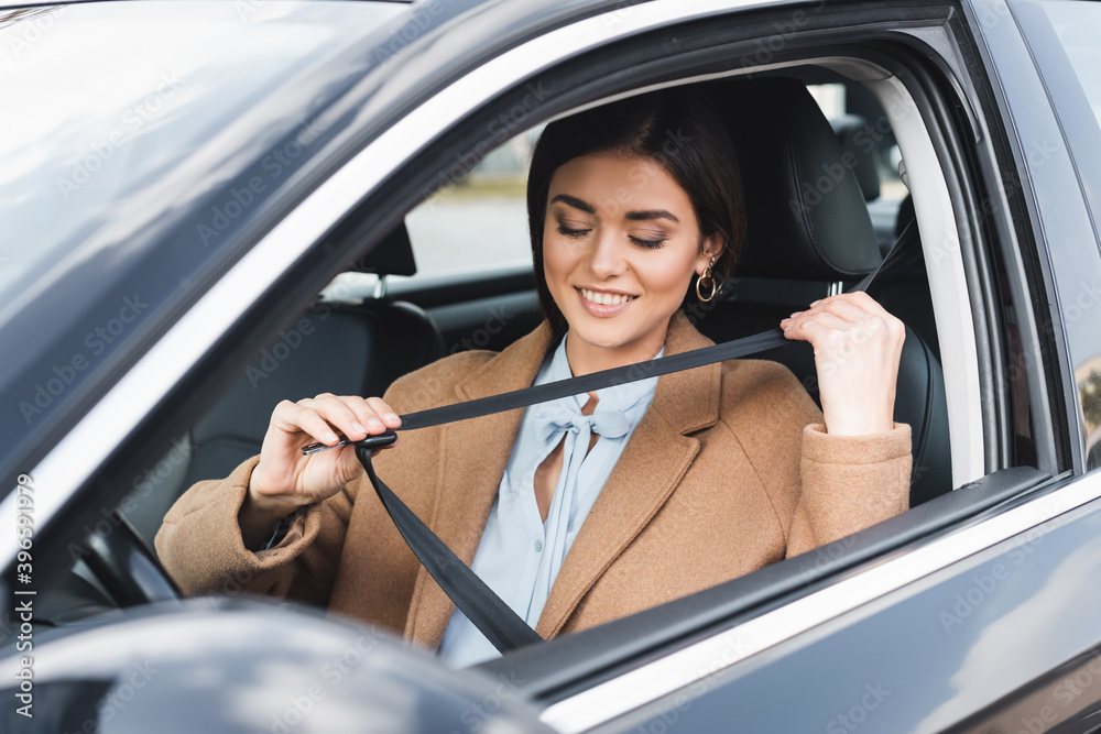 woman in autumn outfit putting on safety belt while sitting in car on blurred foreground woman in autumn outfit putting on safety belt while sitting in car on blurred foreground